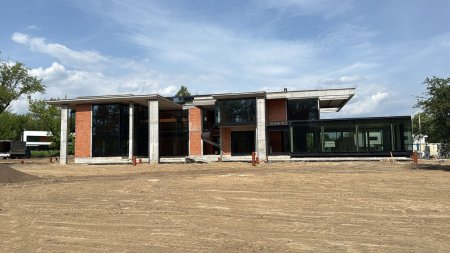 Zdjęcie placu budowy dużej, nowoczesnej rezydencji w stanie surowym zamkniętym. Widoczna masywna konstrukcja żelbetowa, ściany z pustaków ceramicznych oraz zamontowane wielkopowierzchniowe okna aluminiowe, charakterystyczne dla budownictwa premium.